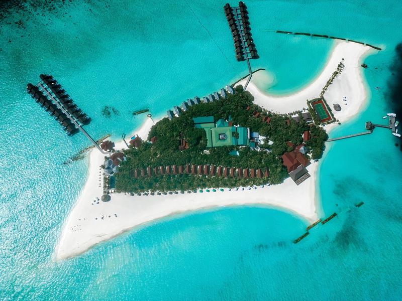 Vista aerea di un'isola tropicale con spiagge di sabbia bianca e bungalow sull'acqua turchese.