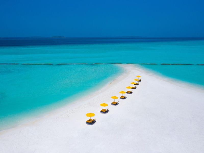 Spiaggia di sabbia bianca con ombrelloni gialli in acqua turchese.