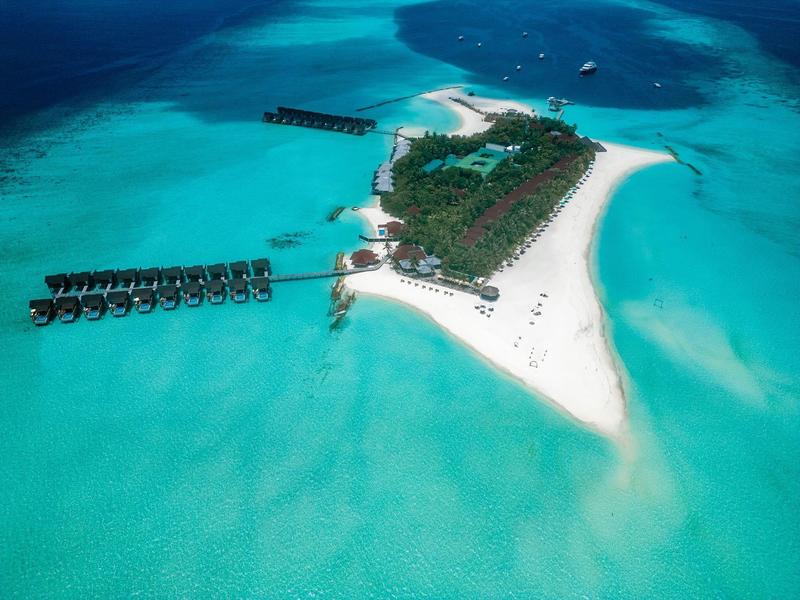 Vista aerea di un'isola tropicale con un resort e moli nell'oceano turchese.