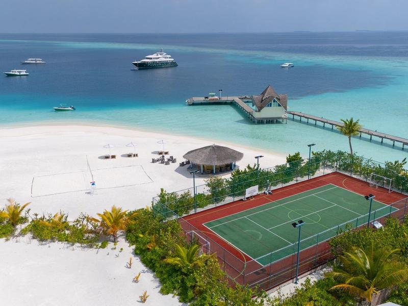 Una spiaggia tropicale con sabbia bianca, acqua turchese limpida, barche e un campo da tennis.