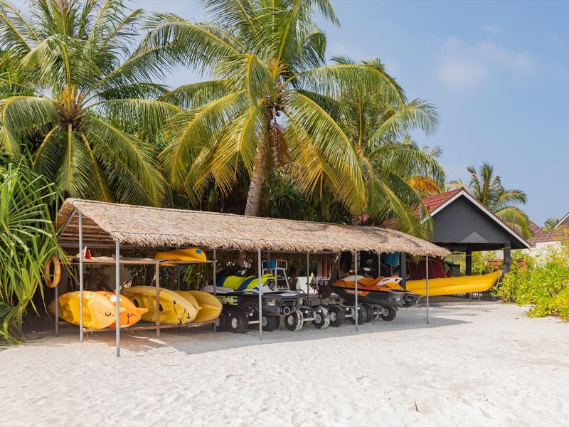 Kajak gialli sotto un tetto di paglia sulla sabbia davanti a palme in una giornata di sole.