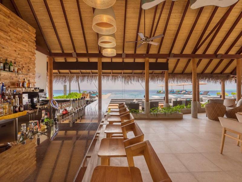 Moderner Strandbarbereich mit Holzdecke, Barstühlen und Blick aufs Meer durch große Fenster.