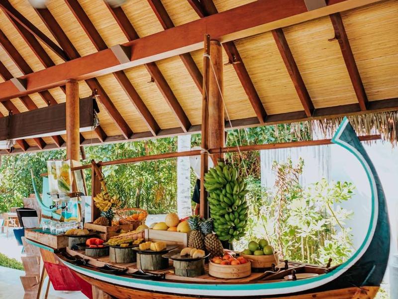 Holzboot mit Buffet, umgeben von tropischen Pflanzen, unter einem Dach mit sichtbaren Trägern.