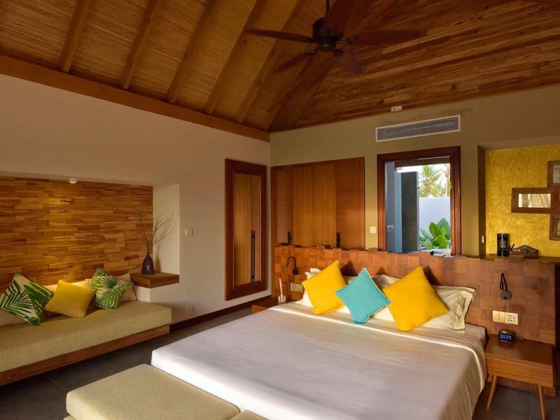 Geräumiges Schlafzimmer mit Holzwänden, Decke, Bett mit bunten Kissen und gemütlicher Sitzbank.