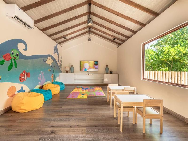 Kinderzimmer mit bunten Sitzsäcken, niedrigem Tisch, Stühlen und großem Fenster mit Blick ins Grüne.