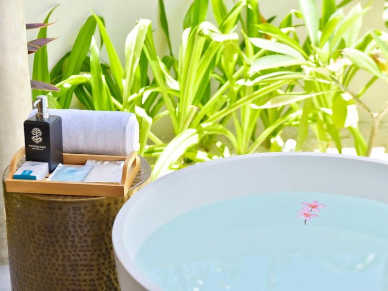 Freistehende runde Badewanne mit Wasser, neben grünem Pflanzenhintergrund und Korb mit Handtüchern.