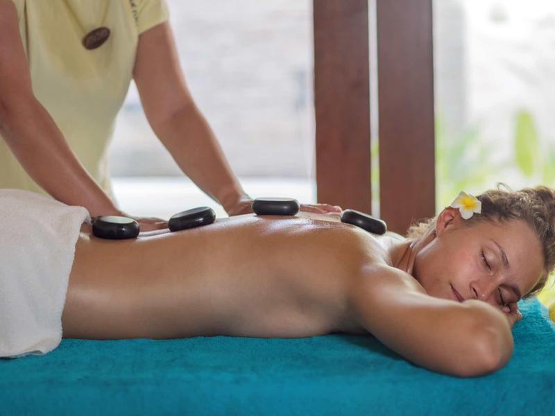 Frau liegt entspannt auf Massageliege, Hot Stones auf Rücken, helle und ruhige Umgebung.