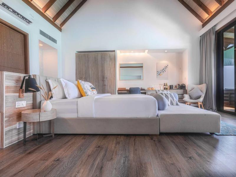 Modernes Schlafzimmer mit Holzboden, Doppelbett, großem Fenster und gemütlicher Sitzbank am Fußende.