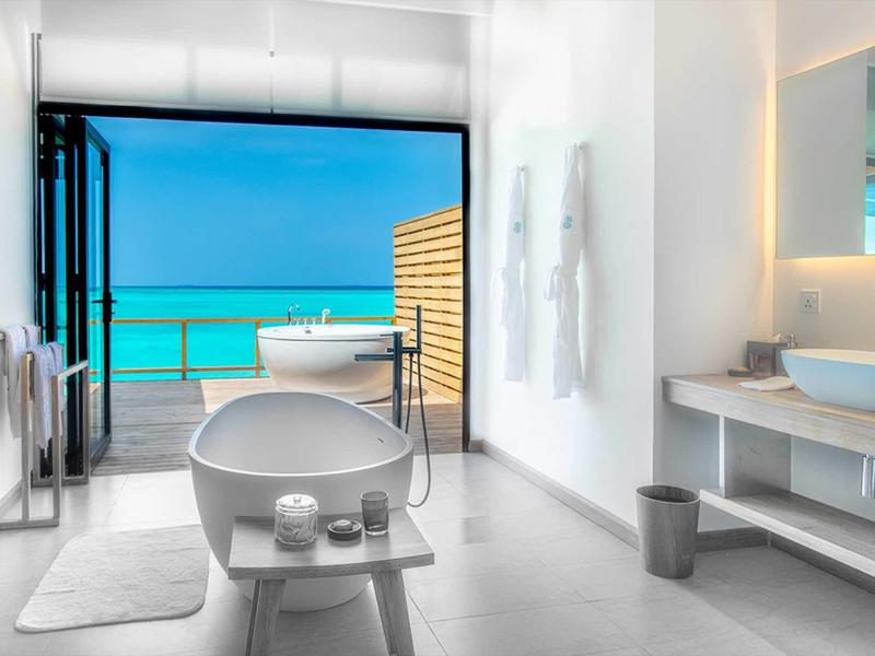 Helles Badezimmer mit freistehender Badewanne, großem Fenster zum Meer und modernen weißen Möbeln.