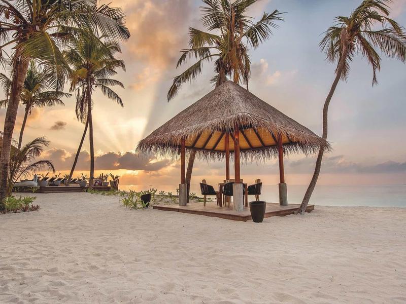 Strand mit Palmen, einer Strohhütte und ruhigem Meer bei Sonnenuntergang.