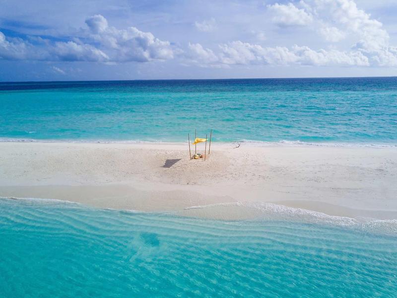Sandinsel mit klarem türkisfarbenem Wasser, weißem Sand und einem gelben Sonnenschirm.