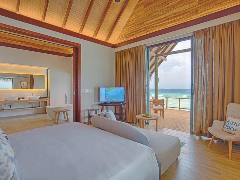 Helles Schlafzimmer mit Holzdecke, Sofa, TV und Blick auf Terrasse und Meer bei Tageslicht.