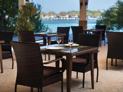 Outdoor restaurant with set tables and a view of water and huts in the background.