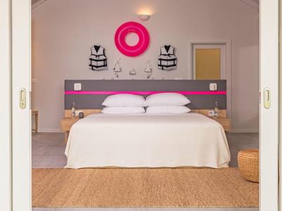 Moderne slaapkamer met tweepersoonsbed, twee fauteuils en roze wanddecoratie.