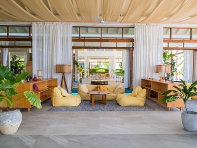 Lichte, moderne lounge met fauteuils, meubels in houtkleur en grote planten.