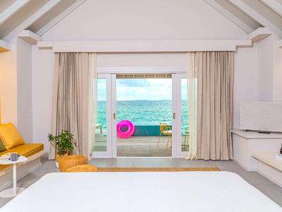 Licht ingericht hotelkamer met zeezicht en toegang tot een terras met zitruimte.