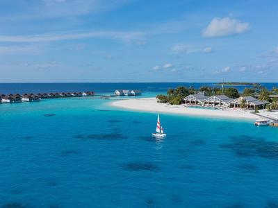 Blauwe zee met zeilboot voor een wit zandstrand en bungalowhotel.