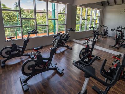 Interior view of a gym room with several stationary bikes on wooden floor and large windows.
