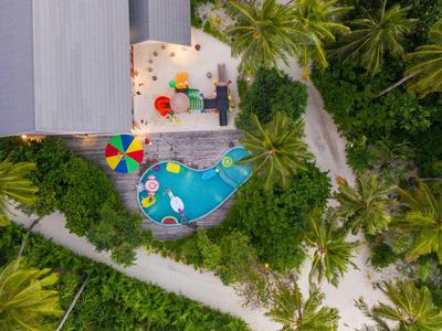 Luchtfoto van een tropisch zwembad met kleurrijke parasols omgeven door palmbomen.