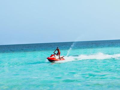 A person rides a red jet ski on the clear blue sea under a blue sky.