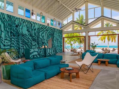 Lichte woonkamer met grote ramen, turquoise banken en uitzicht op zee.