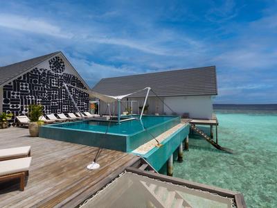 Zwembad op houten steiger boven helder turquoise zee met moderne bungalows en blauwe lucht