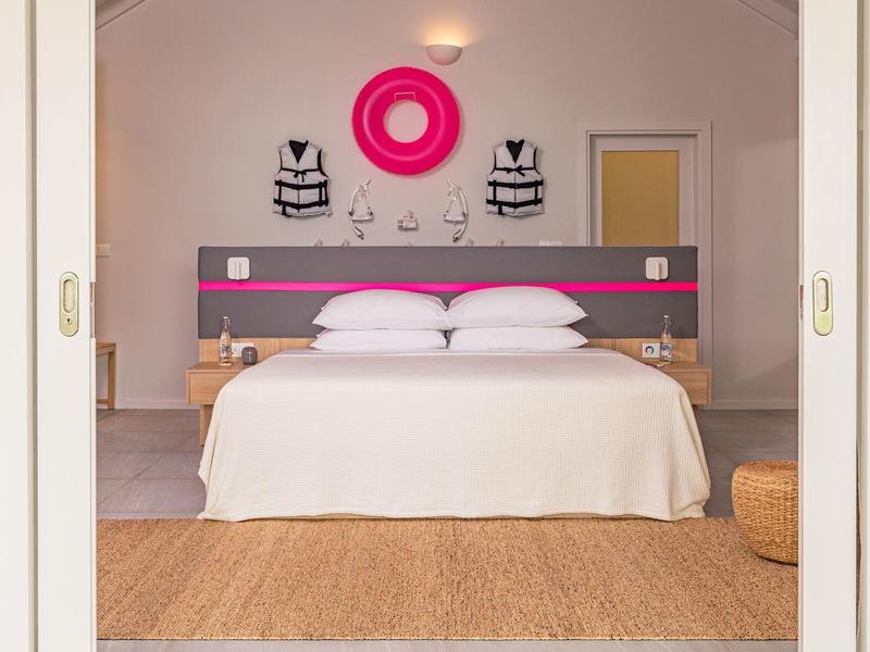 Moderne slaapkamer met tweepersoonsbed, twee fauteuils en roze wanddecoratie.