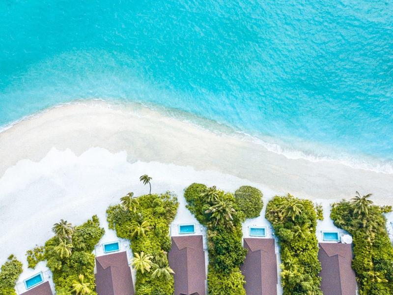 Luchtfoto van strandbungalows met zwembaden aan de turquoise zee en wit zandstrand.