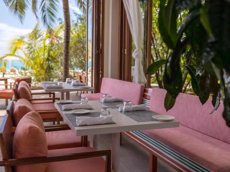 Gezellig terras met roze kussens en buitentafel onder palmbomen.