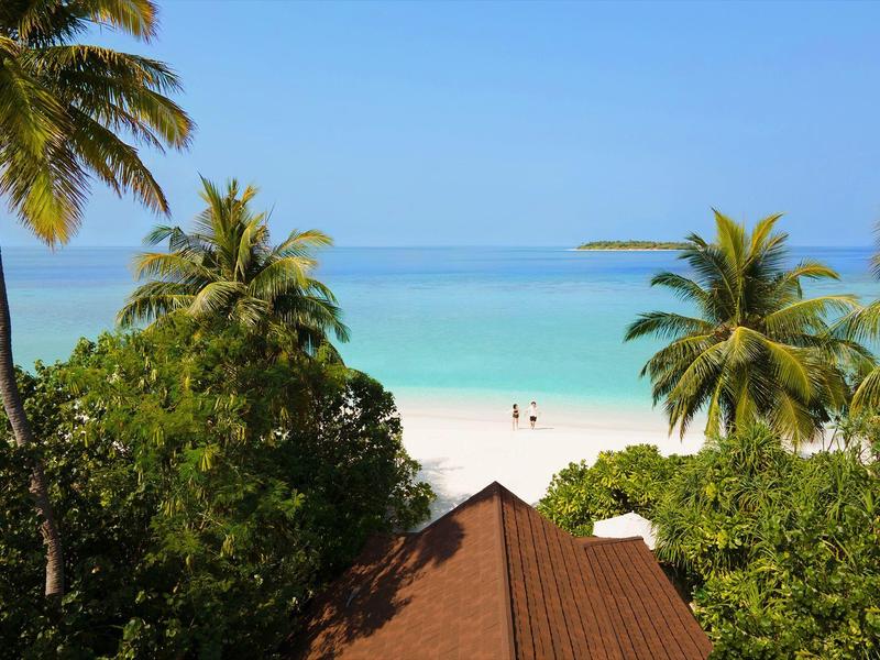Uitzicht op een wit zandstrand met turquoise water en palmbomen, onderdeel van een hotel of resort.