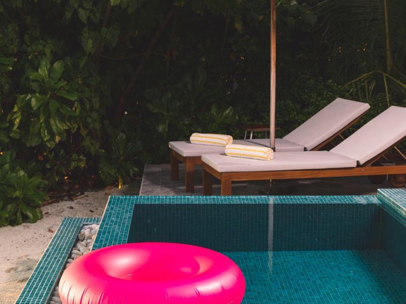 Zwembad met roze zwemring, ligstoelen en parasol voor dichte begroeiing.