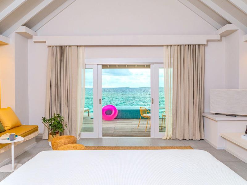Licht ingericht hotelkamer met zeezicht en toegang tot een terras met zitruimte.