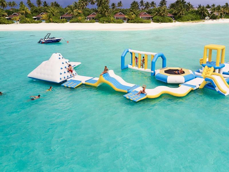 Opblaasbaar waterpark met glijbanen en klimwand in helderblauwe zee bij tropisch strand