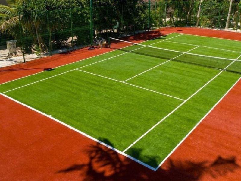 Tennisbaan met rood oppervlak en groen speelveld in een zonnige omgeving.