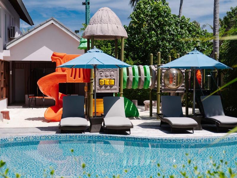 Een zwembad met vier ligstoelen en een kleurrijke speeltuin op de achtergrond.