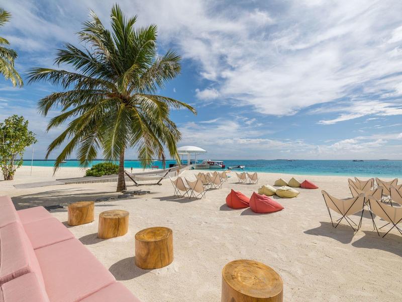 Strand met palmbomen, zitplaatsen en uitzicht op de blauwe zee onder een bewolkte lucht.