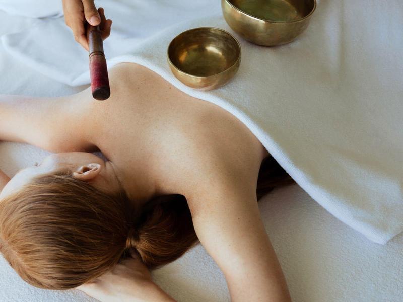 Persoon ligt ontspannen op een tafel terwijl een klankschaalbehandeling wordt gegeven.