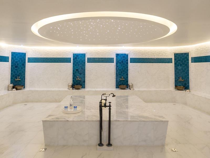 Moderne wellnessruimte met wit marmer, blauwe zuilen en ronde plafondverlichting.