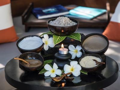 Table noire avec bols de sel, sable et gommage, décorée de fleurs blanches et bougie.