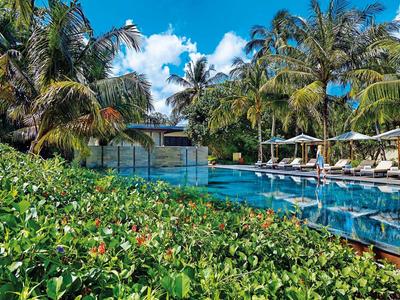 Zone de piscine d'hôtel avec chaises longues et parasols à côté de la végétation tropicale.