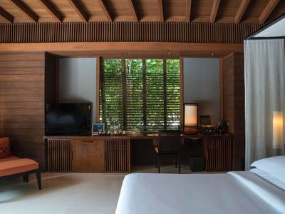 Chambre d'hôtel moderne avec accents en bois, grand lit, coin salon et vue sur des volets verts extérieurs