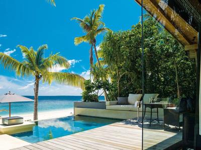 Vue luxueuse de terrasse avec piscine, jardin de palmiers et plage sous un ciel bleu