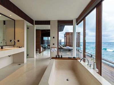 Salle de bain luxueuse avec baignoire autoportante et grande fenêtre en verre donnant sur la mer.