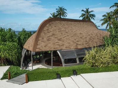 Bâtiment moderne à forme organique avec toit de chaume parmi des palmiers et une végétation luxuriante.