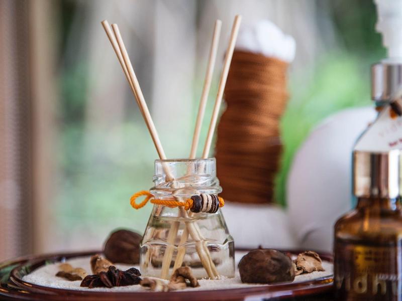 Bâtonnets parfumés dans un petit verre sur un plateau avec des objets décoratifs en arrière-plan.