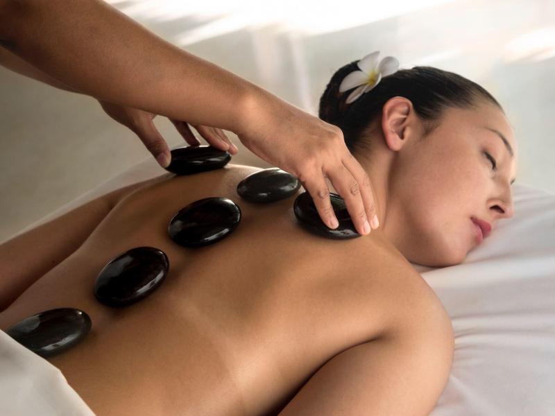 Femme allongée détendue avec des pierres chaudes sur le dos pour un massage bien-être.