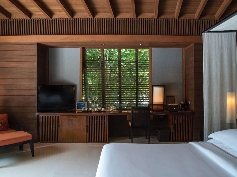 Chambre d'hôtel moderne avec accents en bois, grand lit, coin salon et vue sur des volets verts extérieurs