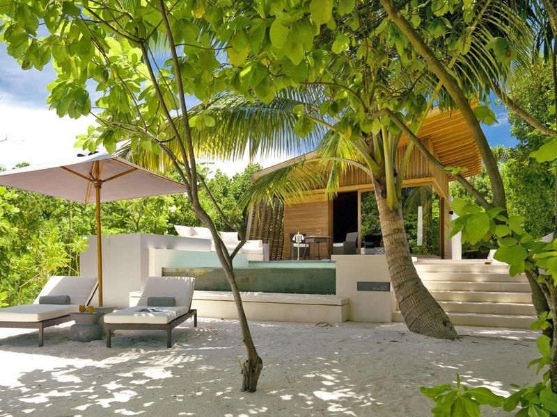 Villa de plage avec piscine, chaises longues et parasol, entourée d'une végétation tropicale luxuriante.