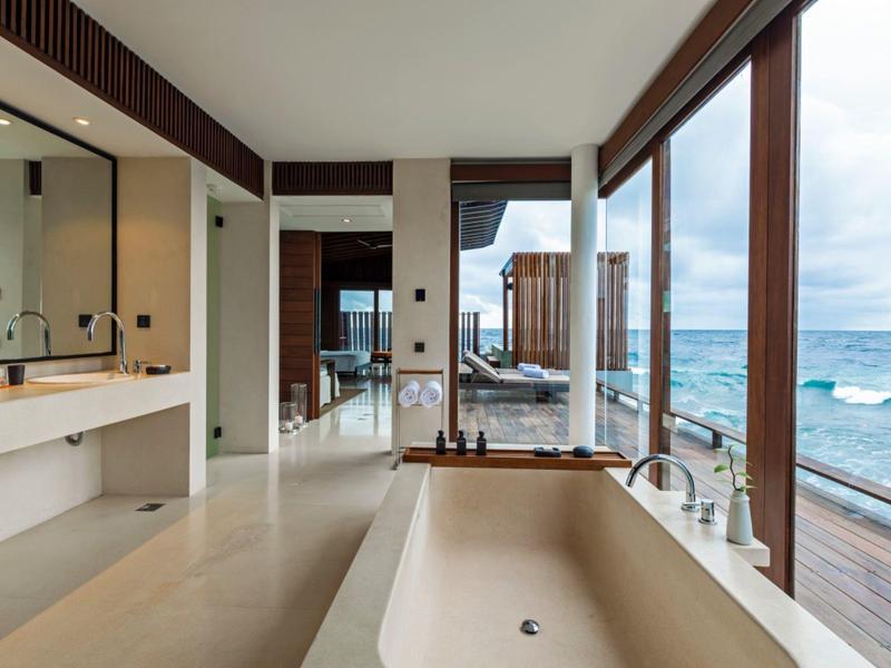 Salle de bain luxueuse avec baignoire autoportante et grande fenêtre en verre donnant sur la mer.