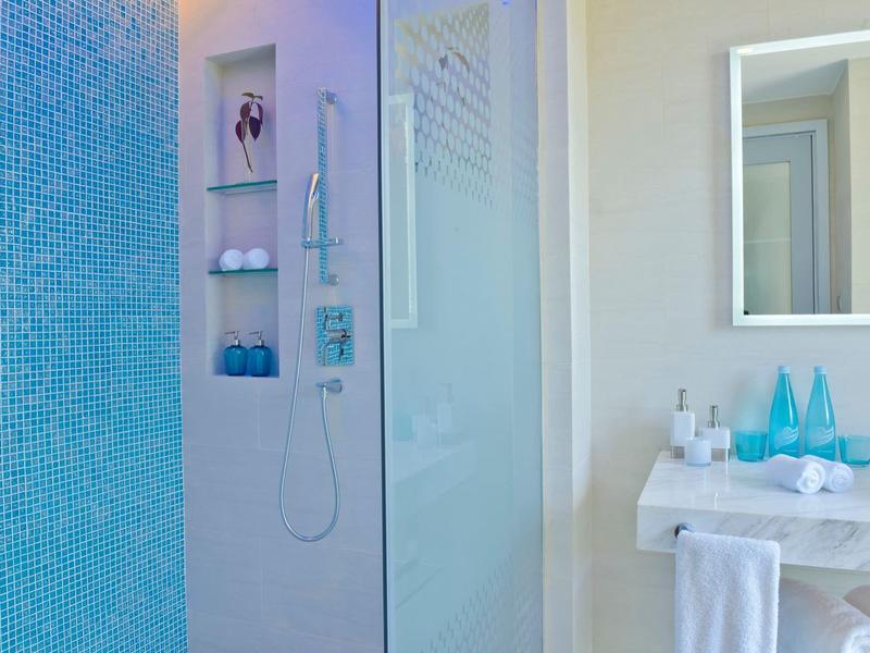 Modernes Badezimmer mit blauen Mosaikfliesen, Glasdusche und weißem Waschbecken mit Handtuchhalter.